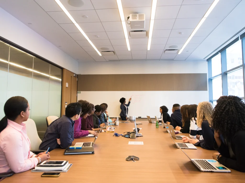 A facilitator at a whiteboard in front of a full meeting table
